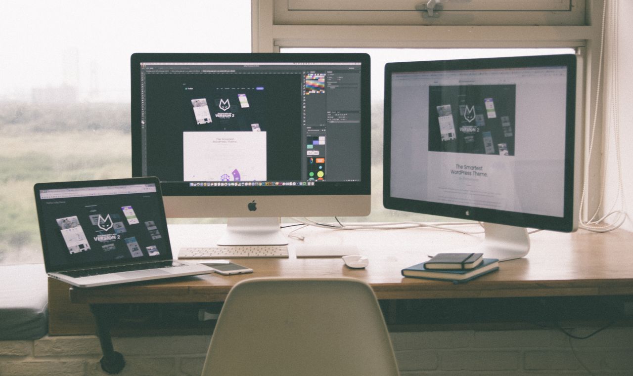 Elegantní a efektivní pracovní prostředí s více monitory, notebookem a chytrým telefonem, které představuje webdesignový projekt.
